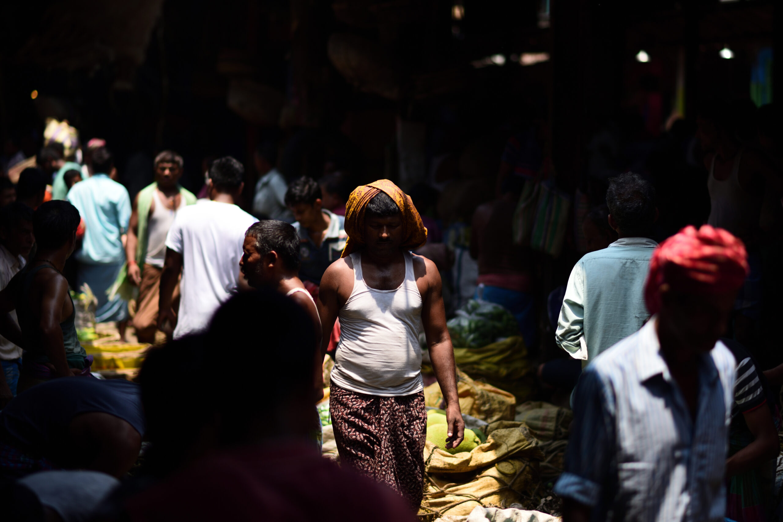 A crowded market in Kolkata India. The market is quite dark with a ray of light through the centre, illuminating a strip of people.