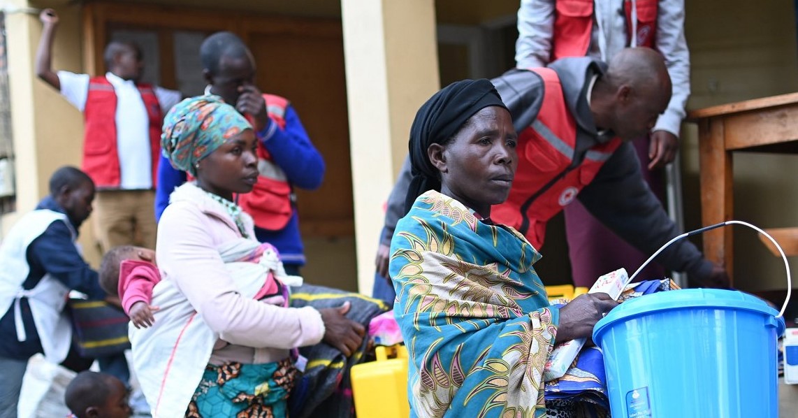 People impacted by the flood in Rwanda stand outside a building with Red Cross workers.