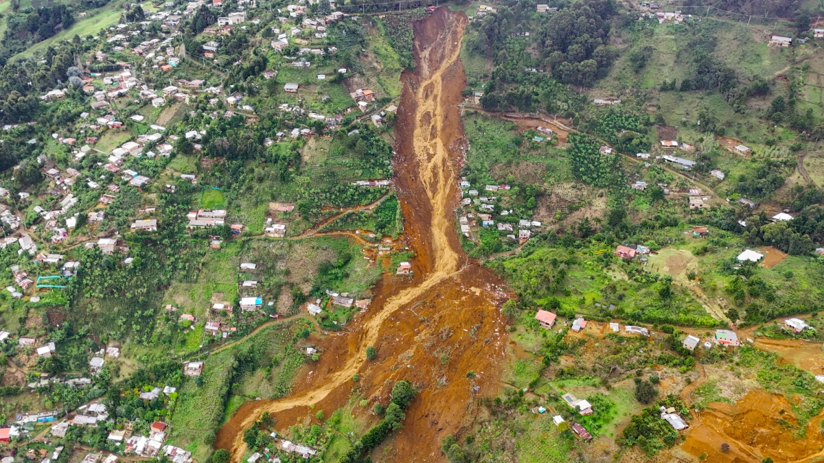 An aerial image of a landslide near Medellin in Colombia. A huge trail of mud and earth cuts down a green hillside, burying homes.
