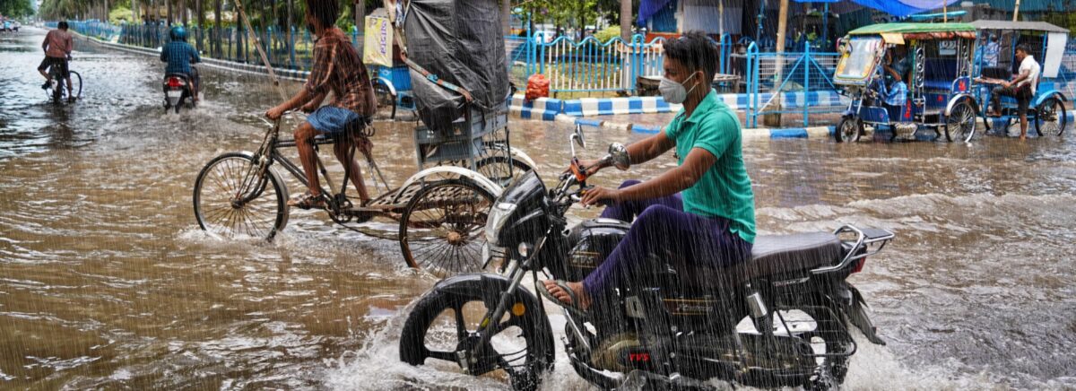 A man rides a motorbike through brown floodwaters.