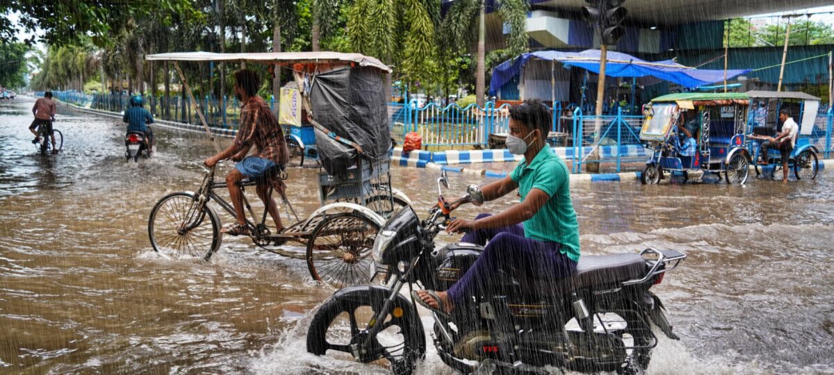 A man rides a motorcycle through brown floodwaters.
