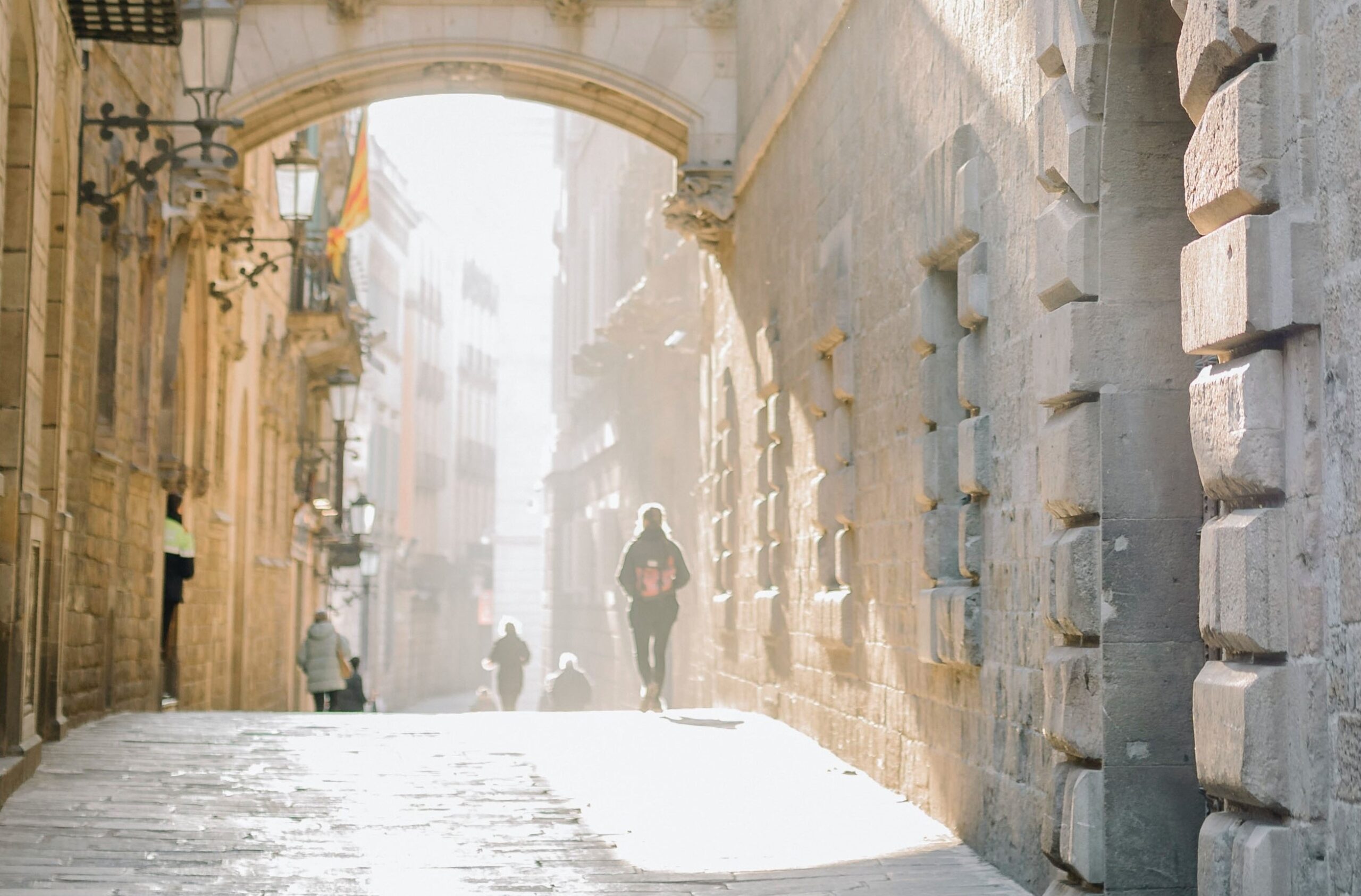 Sun beams into a historic Spanish street as people walk in the distance.