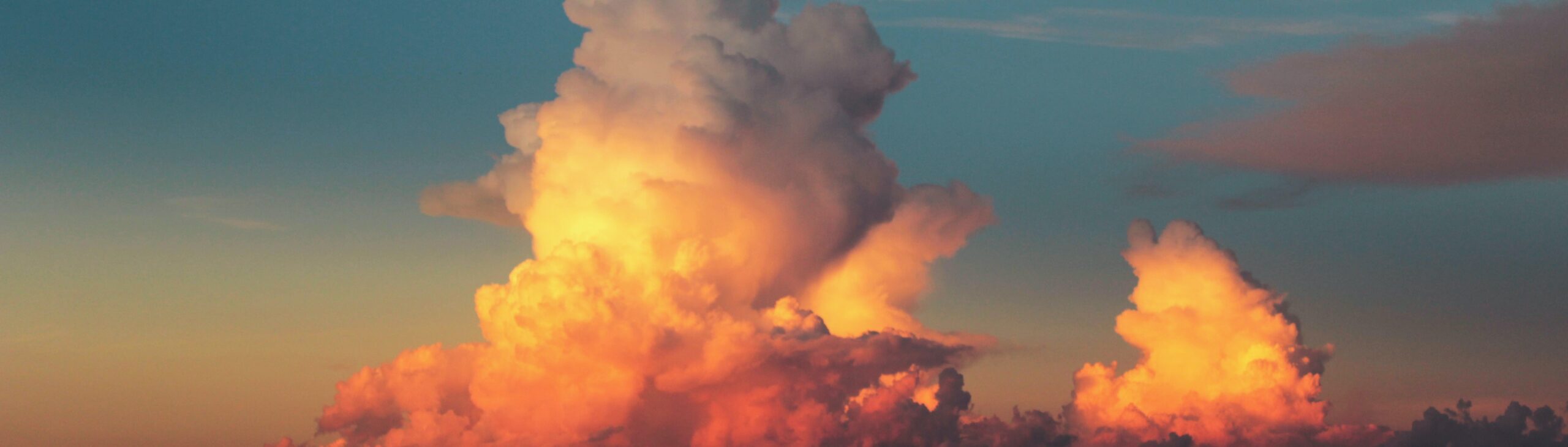 A photo of large clouds at sunset, the sky and clouds coloured orange, white, pink and blue